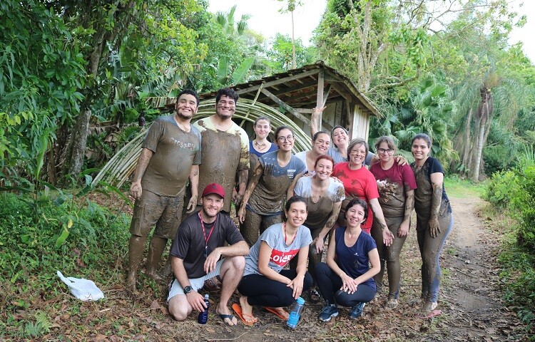 Vários participantes sujos de lama posam para foto em paisagem com árvores